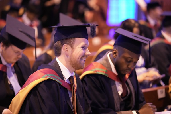 Two male graduates sitting in their caps and gowns.